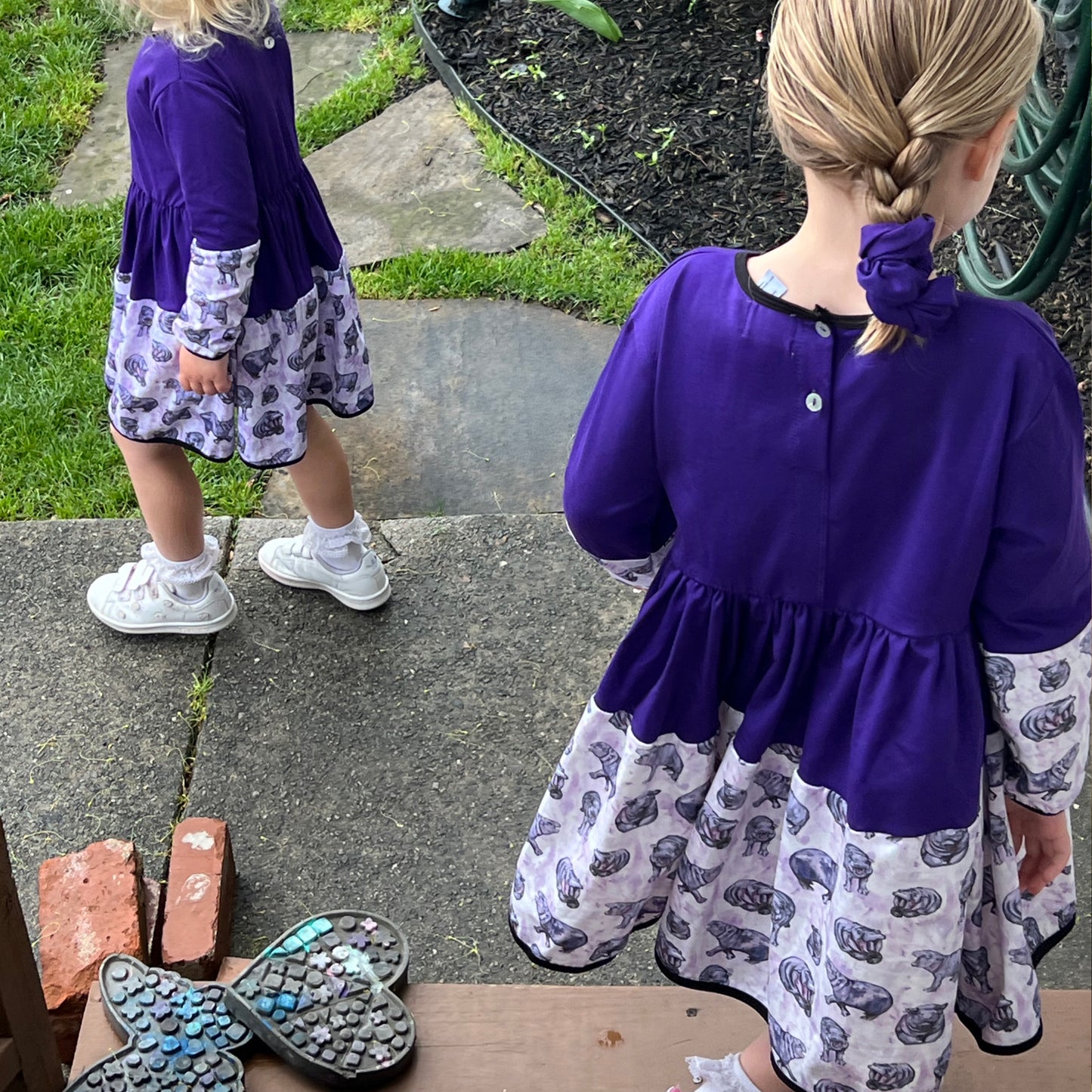 Two little girls in long sleeve purple hippo dresses, featuring a fun print and comfortable fit for play.