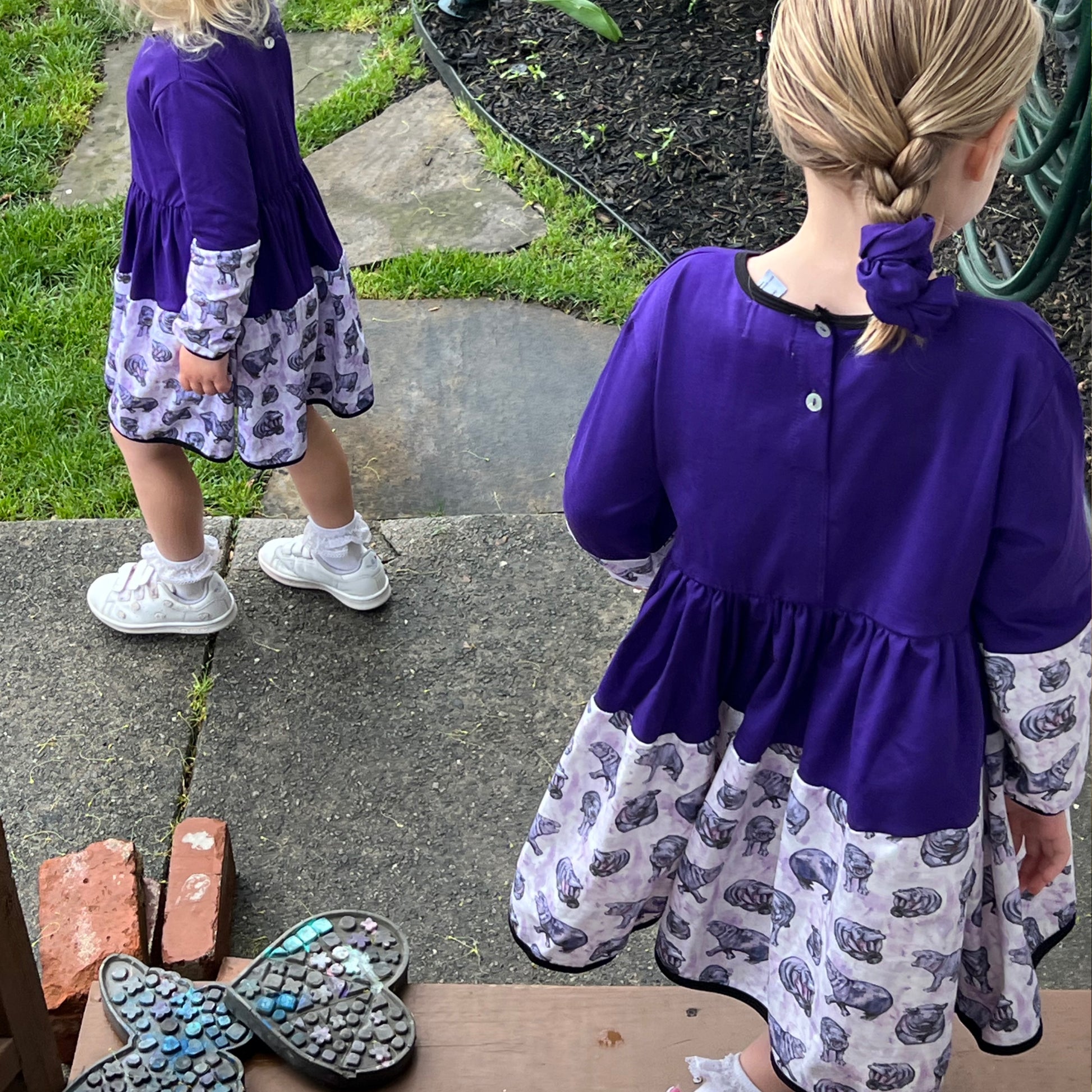Two little girls in long sleeve purple hippo dresses, featuring a fun print and comfortable fit for play.