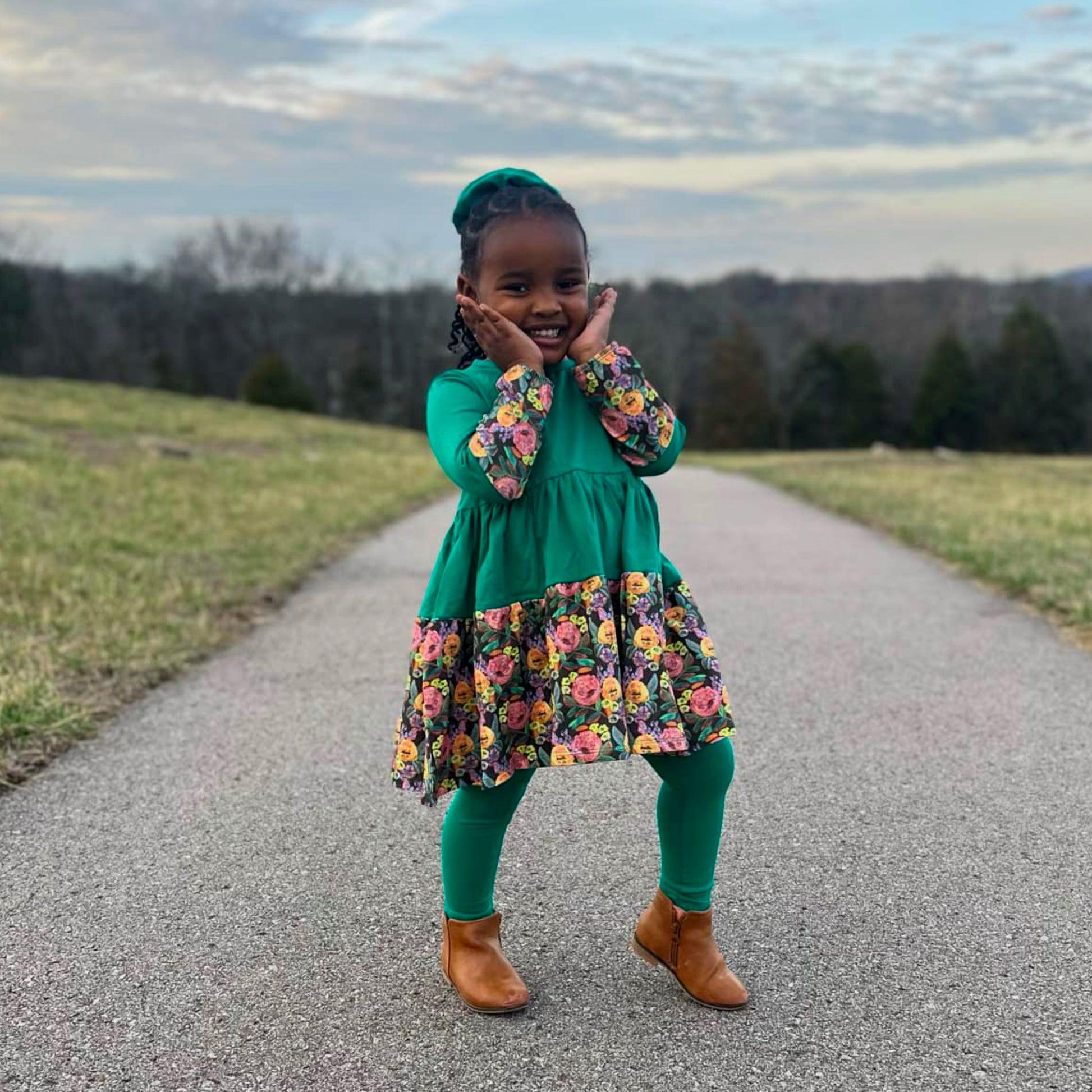 Smiling Girl Green Dress - Child wearing a forest green twirl dress mid-twirl outdoors; soft cotton girls dress by The Pink Picket Fence
