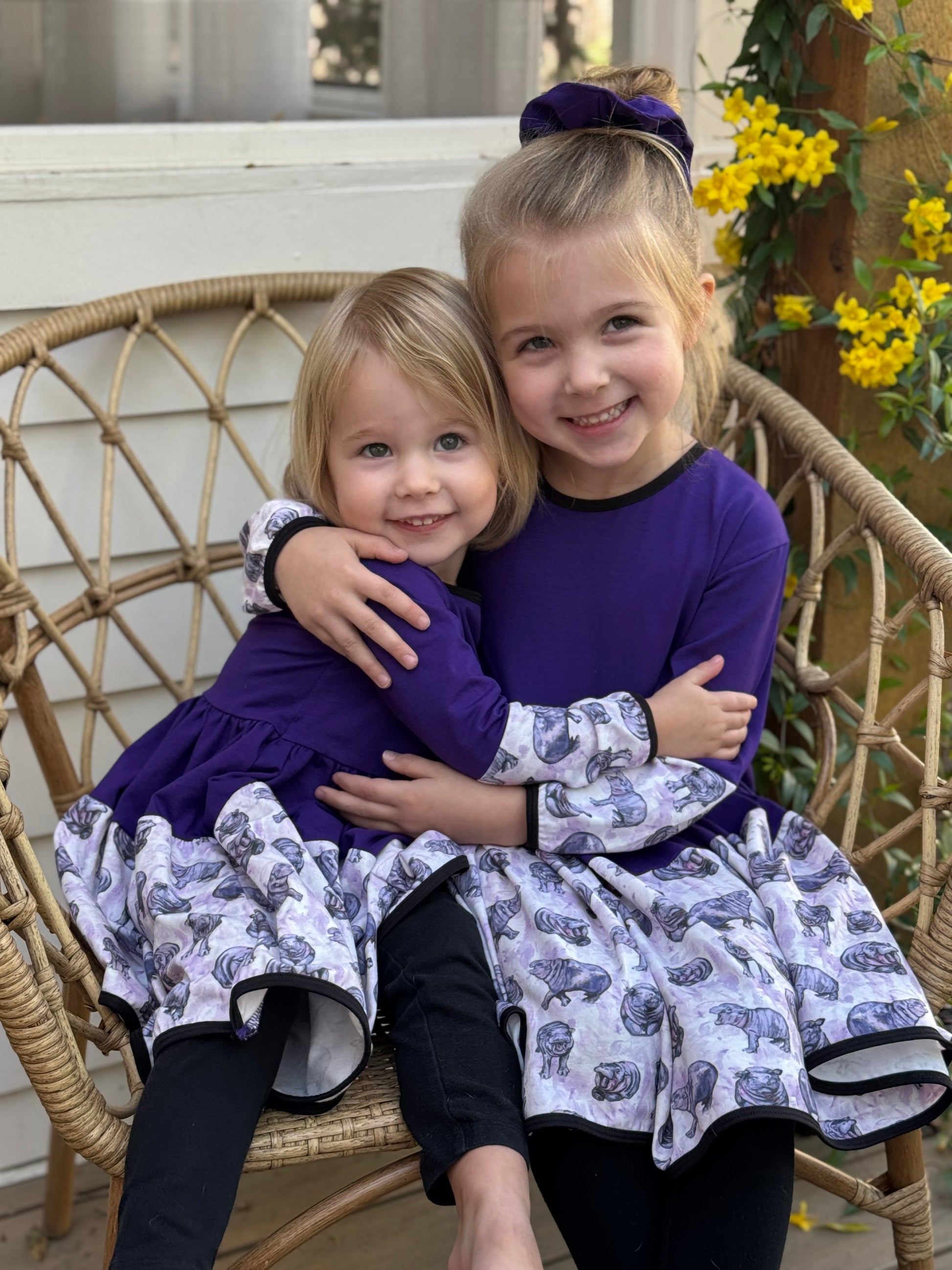Two girls twirling in matching purple hippo dresses, showing off the playful animal print and long sleeves.