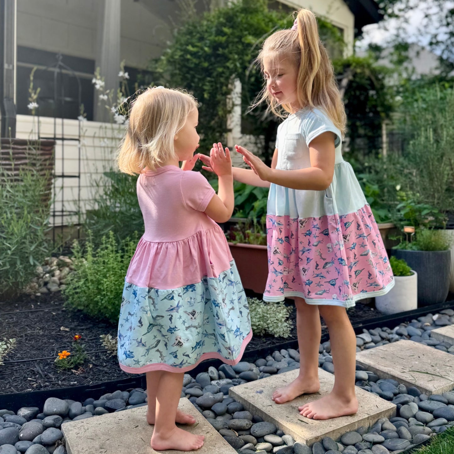 Sisters in coordinating ocean-themed dresses – soft 100% cotton pink and blue shark dresses with playful hand-painted designs