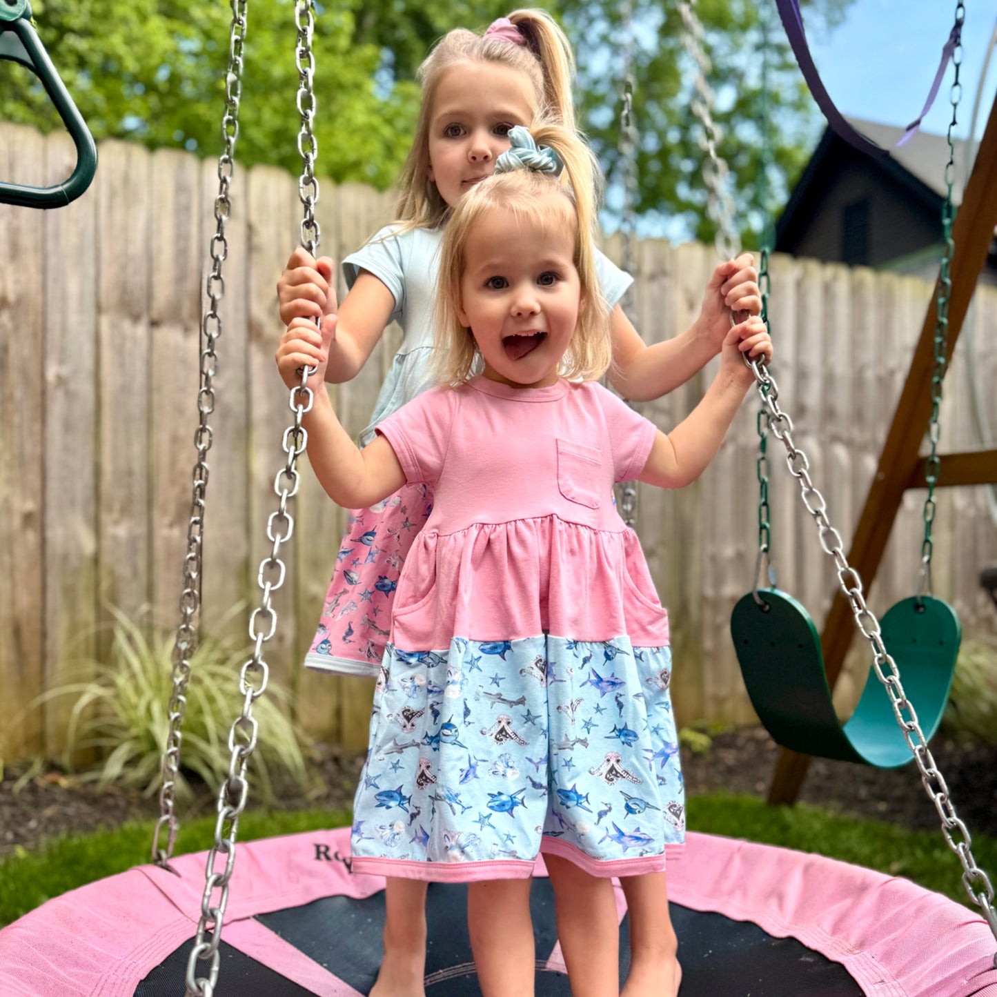 Sisters in coordinating ocean-themed dresses – soft 100% cotton pink and blue shark dresses with playful hand-painted designs