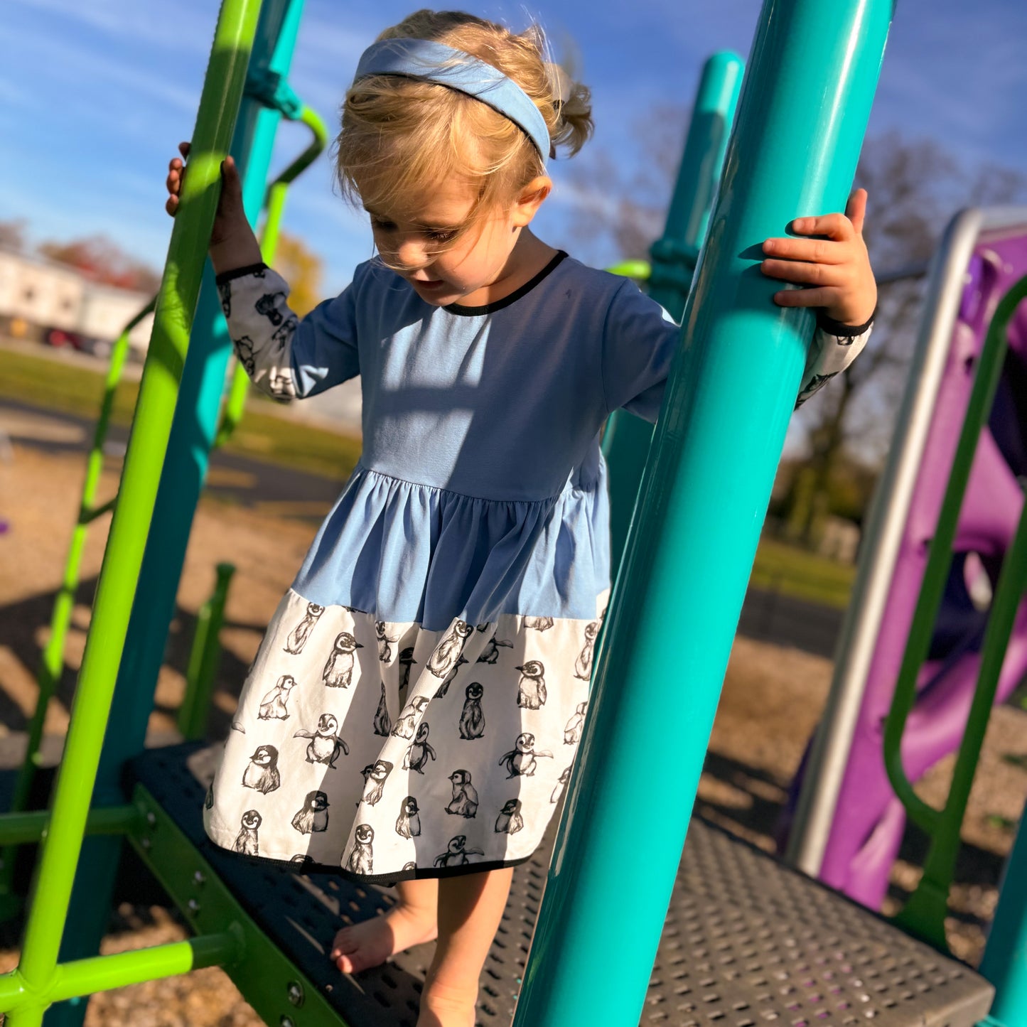 Young Girl at the Park - Young girl spinning in her cotton penguin-print dress during a sunny park day, perfect for play.