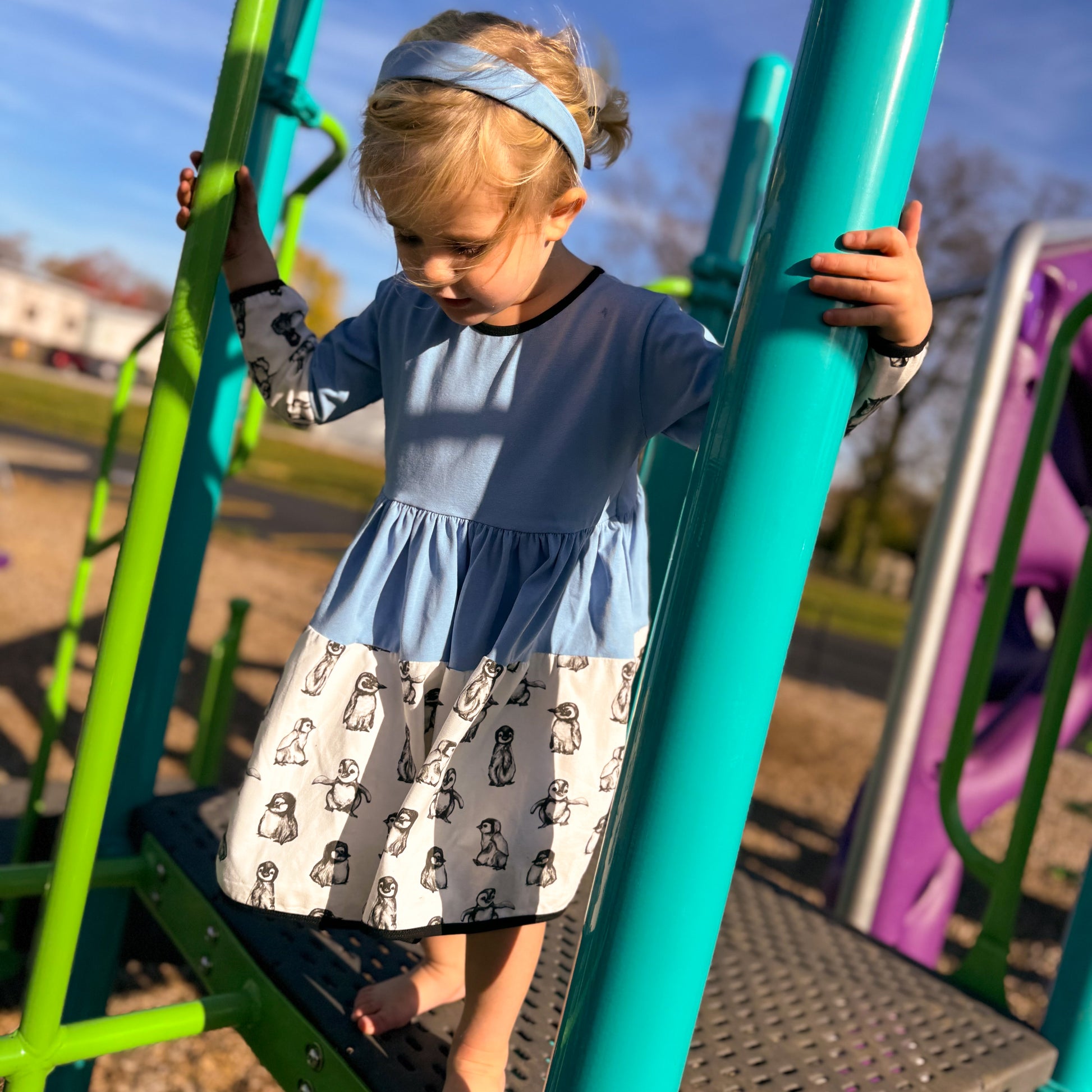 Young Girl at the Park - Young girl spinning in her cotton penguin-print dress during a sunny park day, perfect for play.