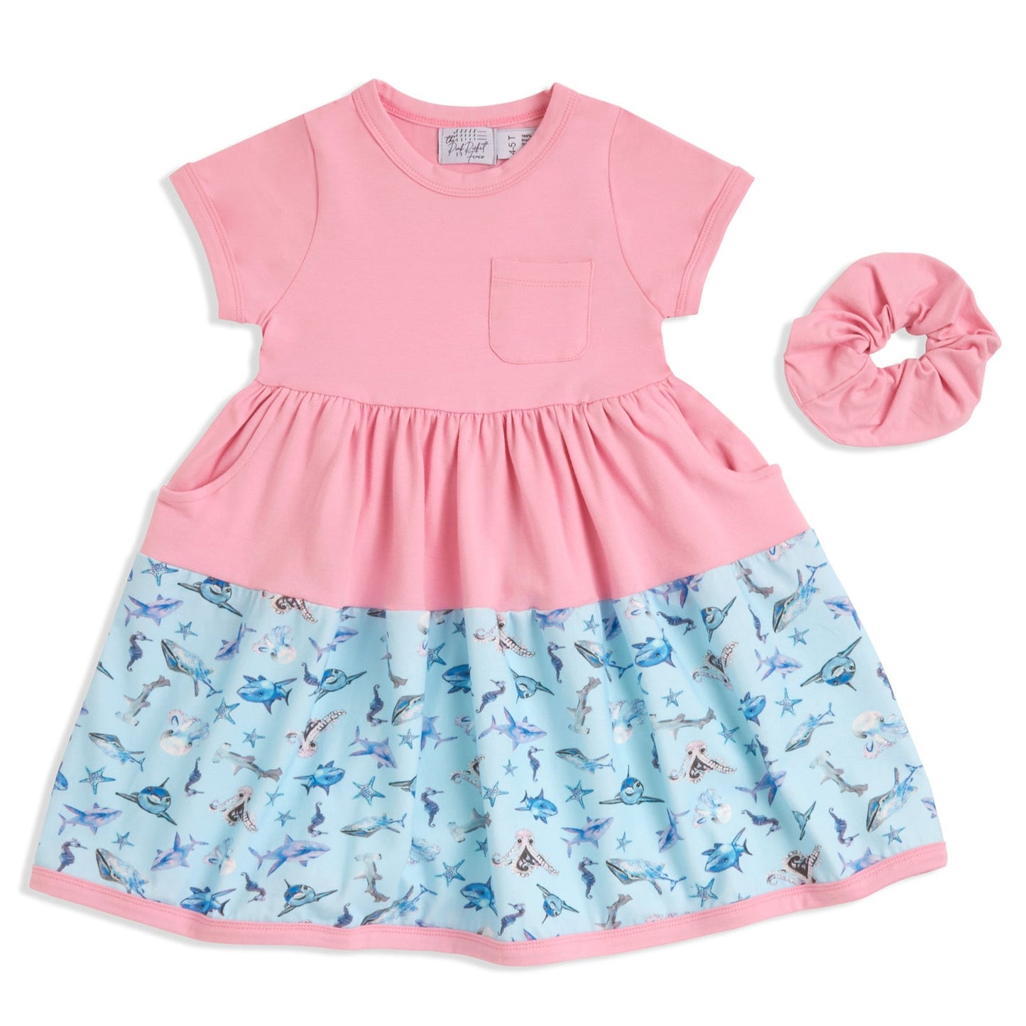 Flat lay of pink Sparky Shark girls dress with matching scrunchie – short-sleeve 100% cotton twirl dress featuring ocean animals like sharks, octopuses, and starfish