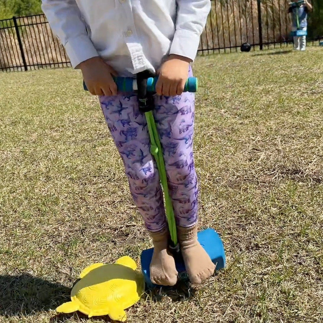 Child on pogo stick playing in purple dino leggings