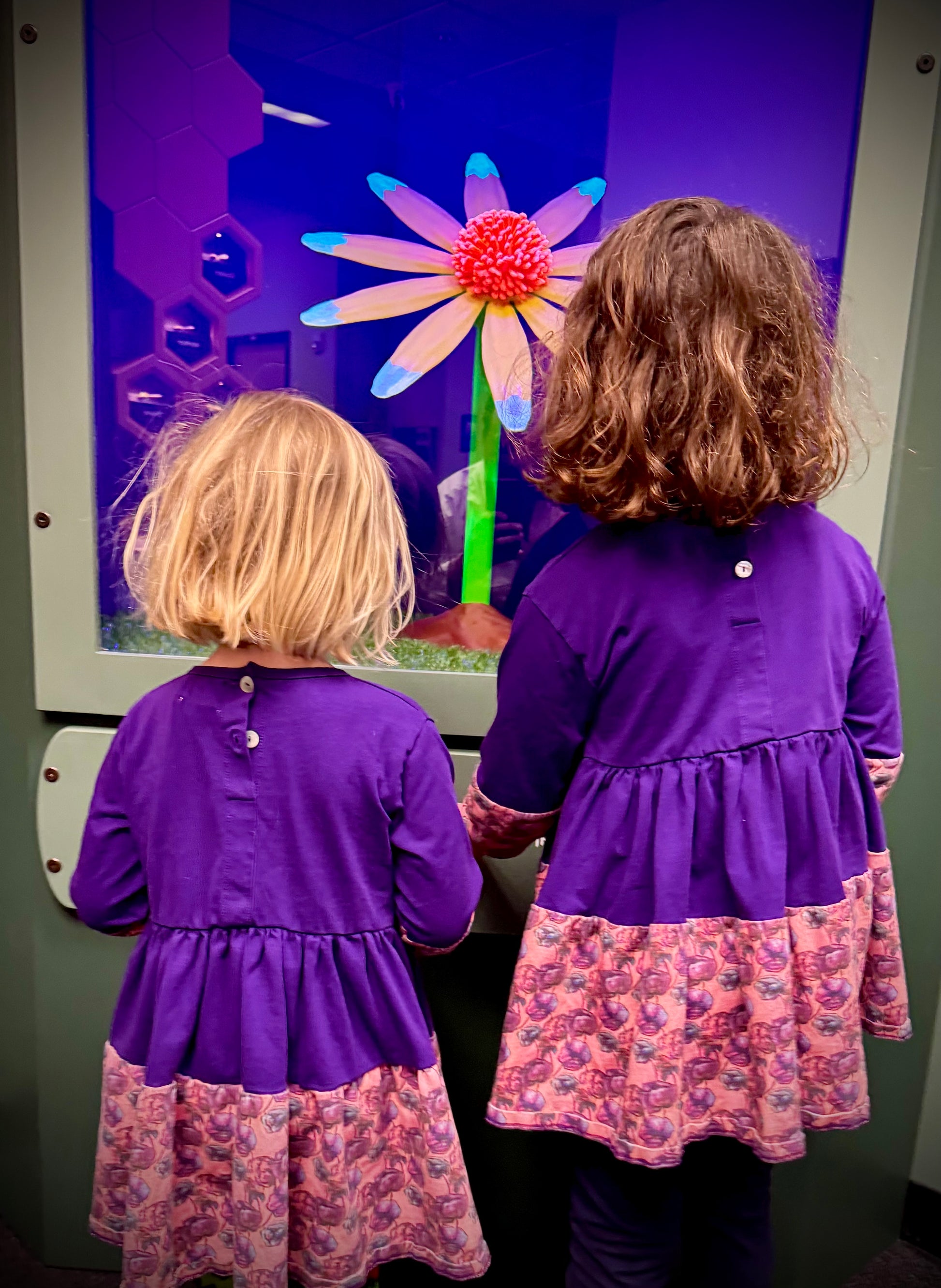 Two girls wearing matching Purple Louise Twirl Dresses standing together in a museum setting, surrounded by artwork.