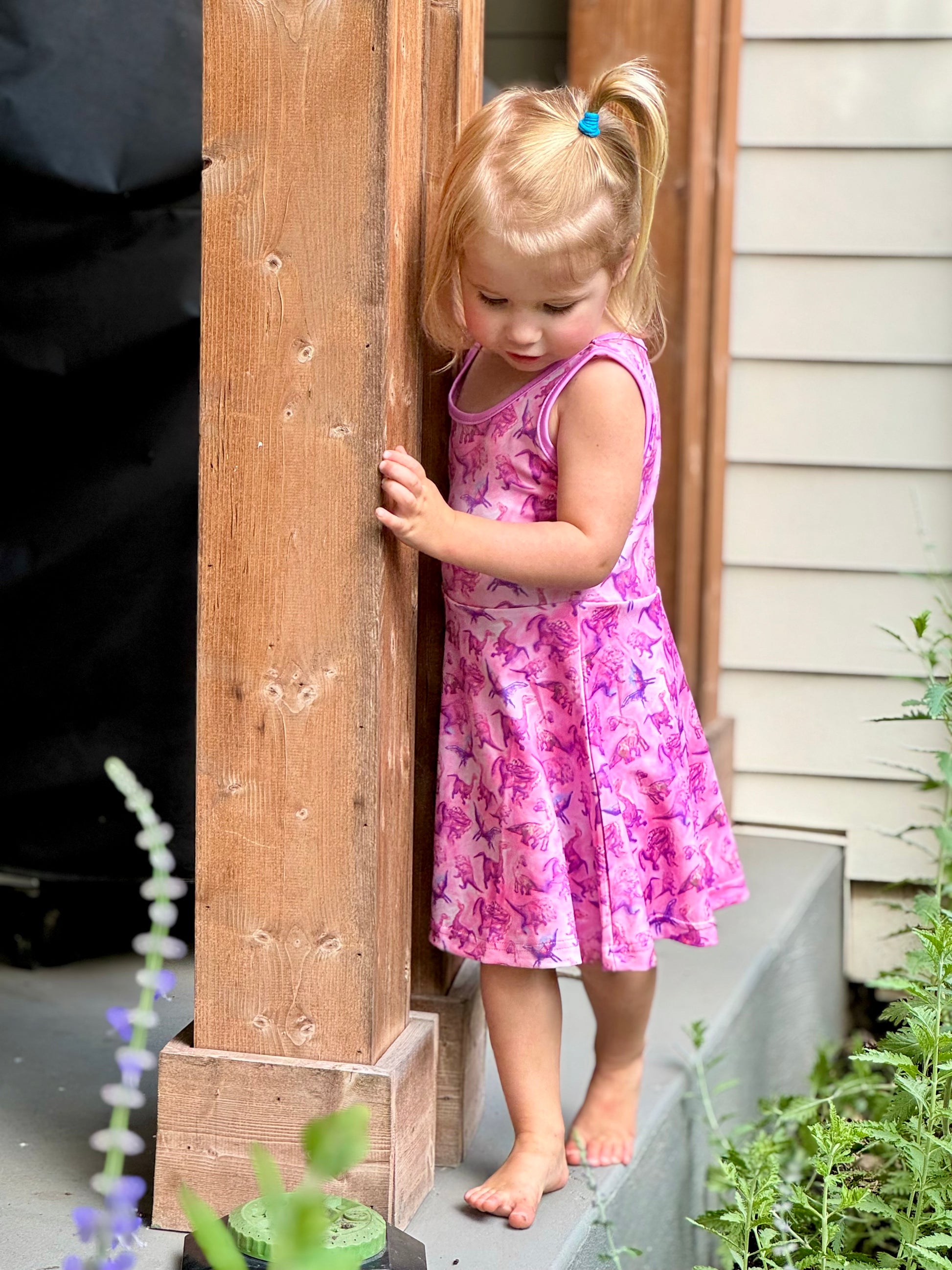 Toddler girl wearing sleeveless pink dino dress while twirling – breathable and stretchy summer outfit for kids