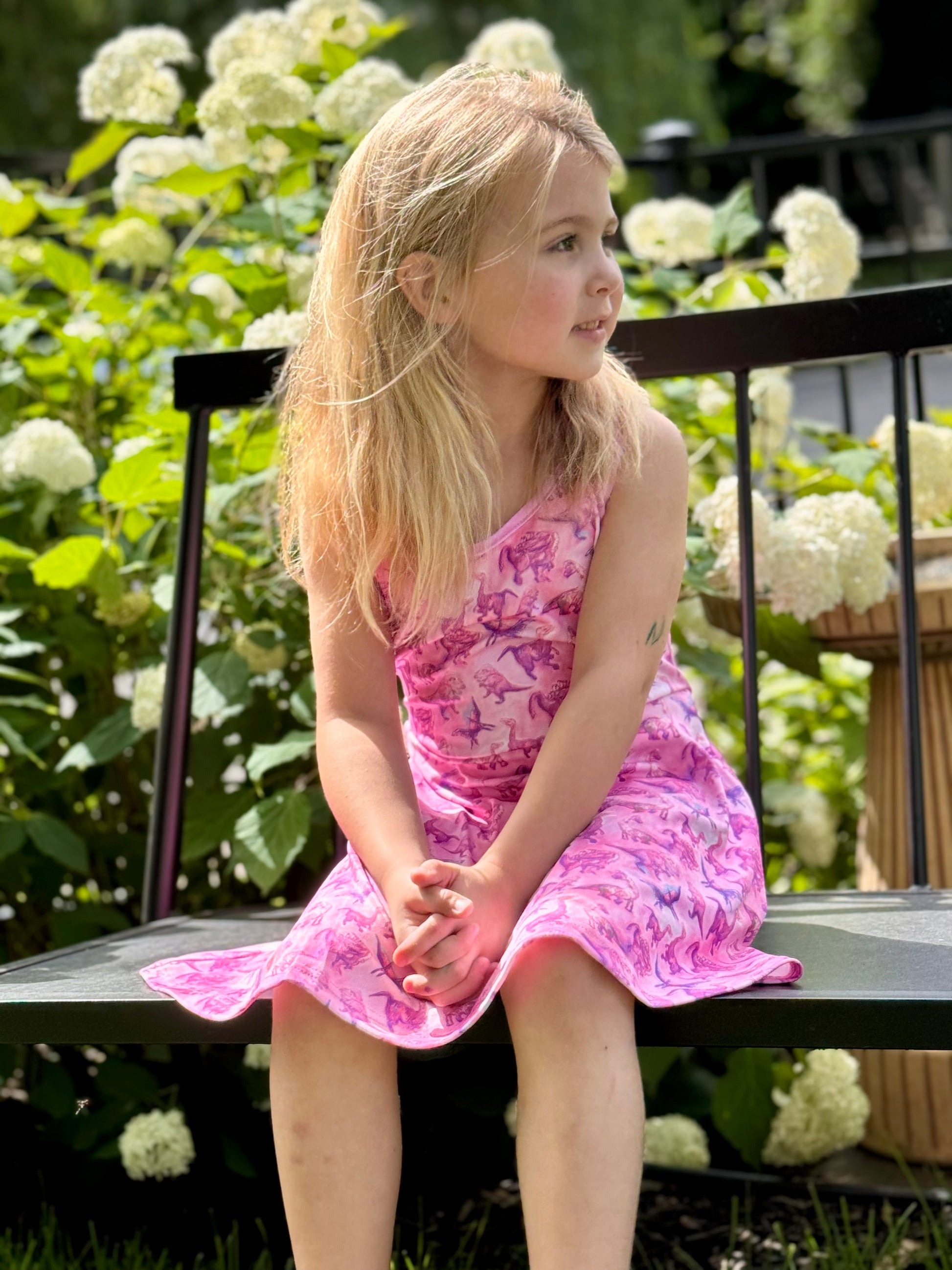 Young girl wearing sleeveless dinosaur dress running through grass – playful toddler clothing for active kids