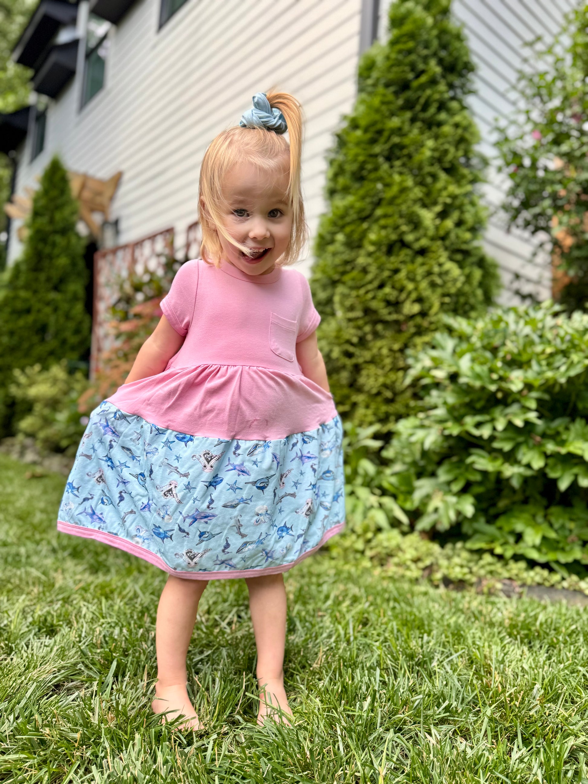 toddler girl wearing blue shark twirl dress with pink top standing on grass soft sensory friendly summer dress for kids