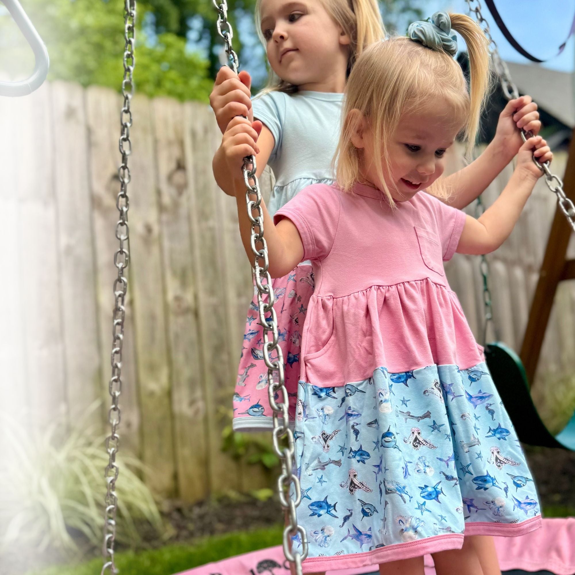 toddler girl wearing soft cotton twirl dress sensory friendly kids clothing playing on swing The Pink Picket Fence